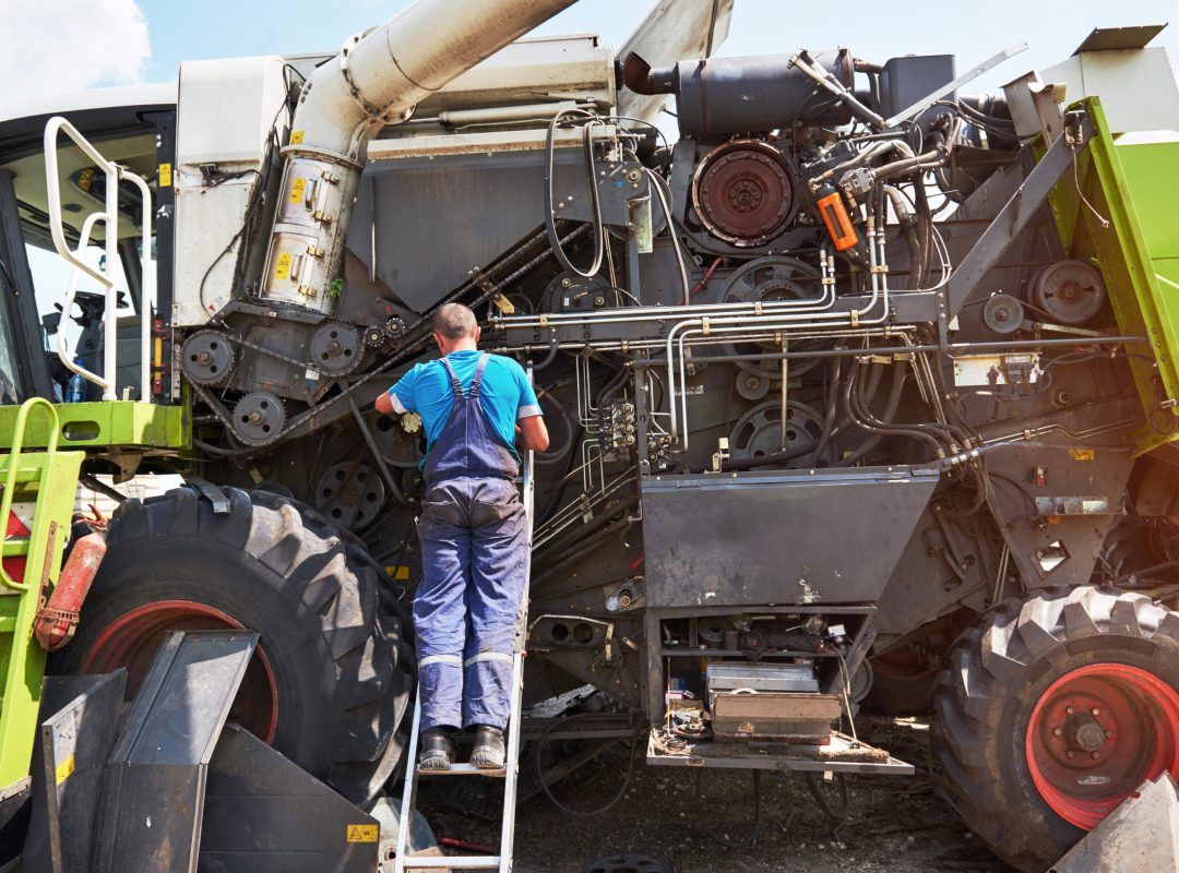 Combine machine service, mechanic repairing motor outdoors